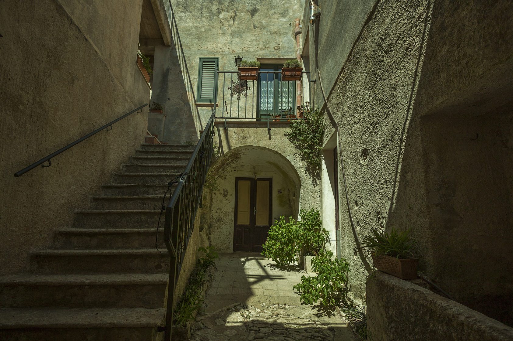 Eine enge mittelalterliche Gasse in Erice, mit grauem Kalksteinpflaster, die sich zu einem fernen Blick auf die sizilianische Küste öffnet.